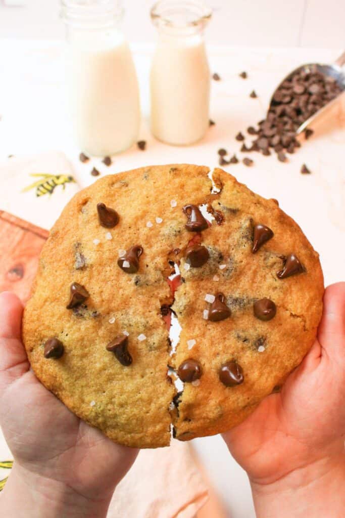 kid hands breaking apart a large chocolate chip cookie.