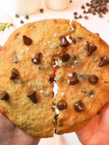 a large chocolate chip cookie being broken in half.