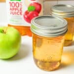 apple jelly in a jar in front of apple juice and fresh apple.