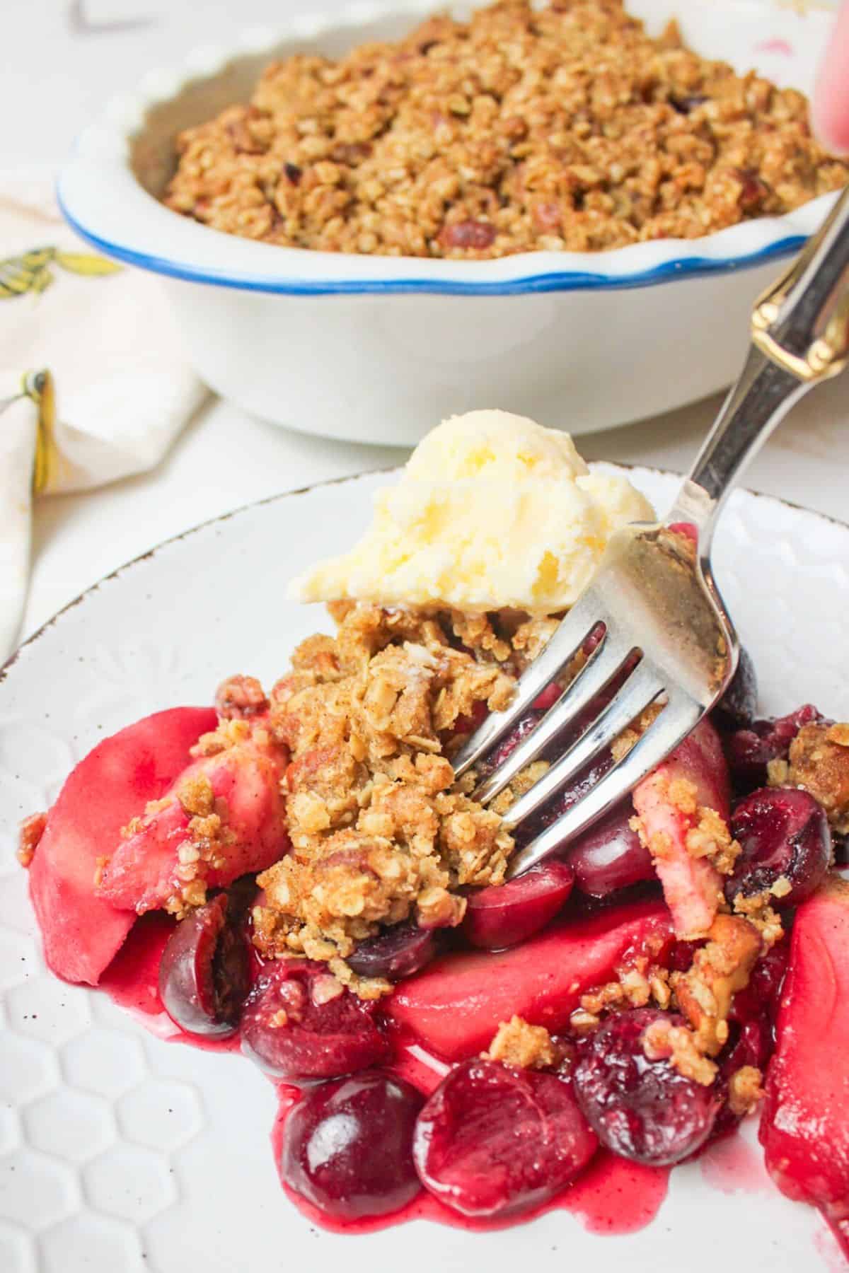 fork stabbing into serving of cherry apple crisp on a plate.