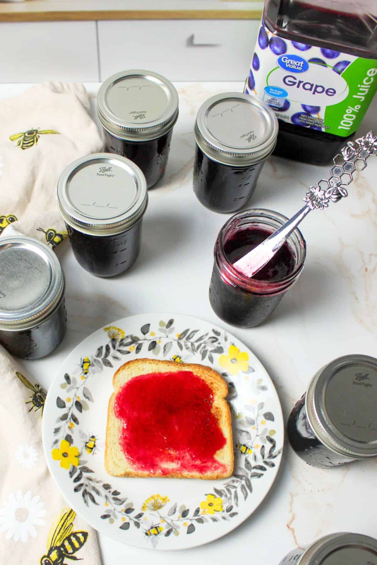 grape jelly spread over toast on a plate with jars of jelly around it.