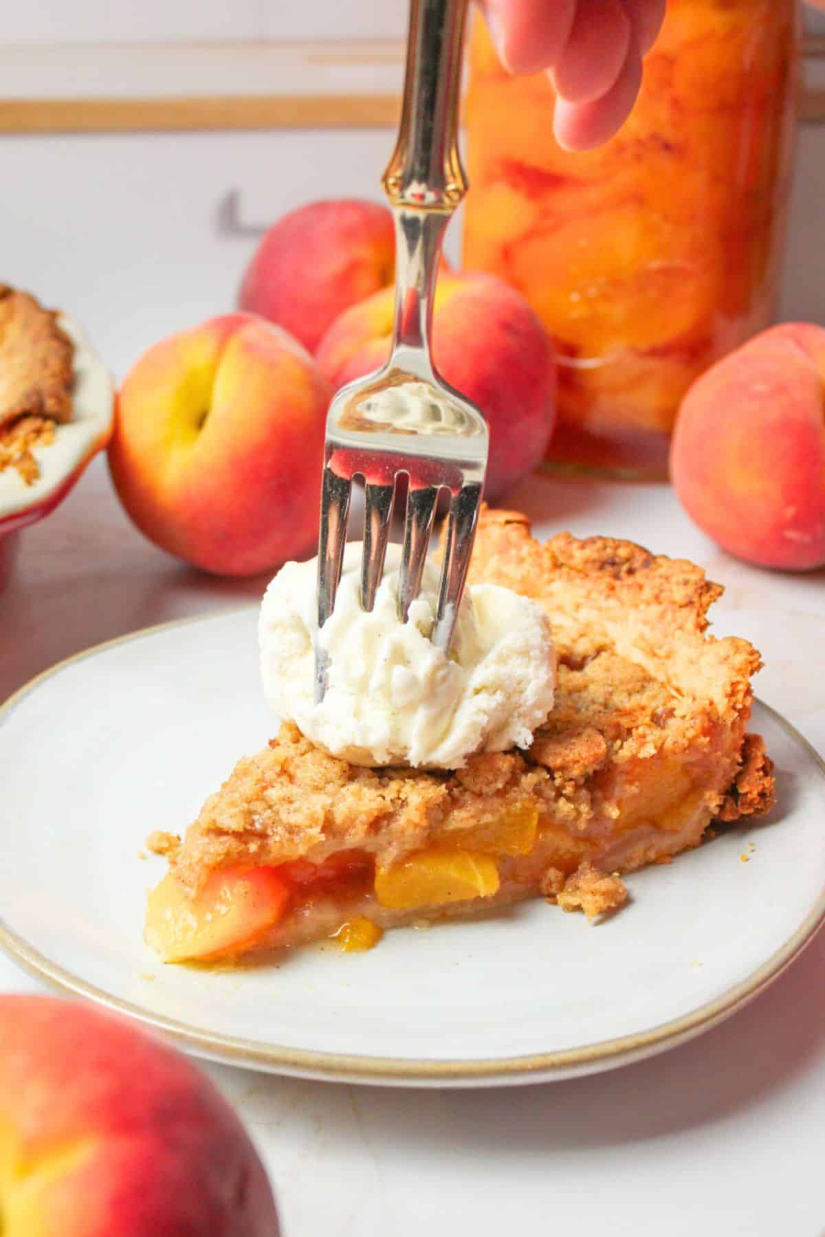 fork into slice of peach crumble pie topped with vanilla ice cream.