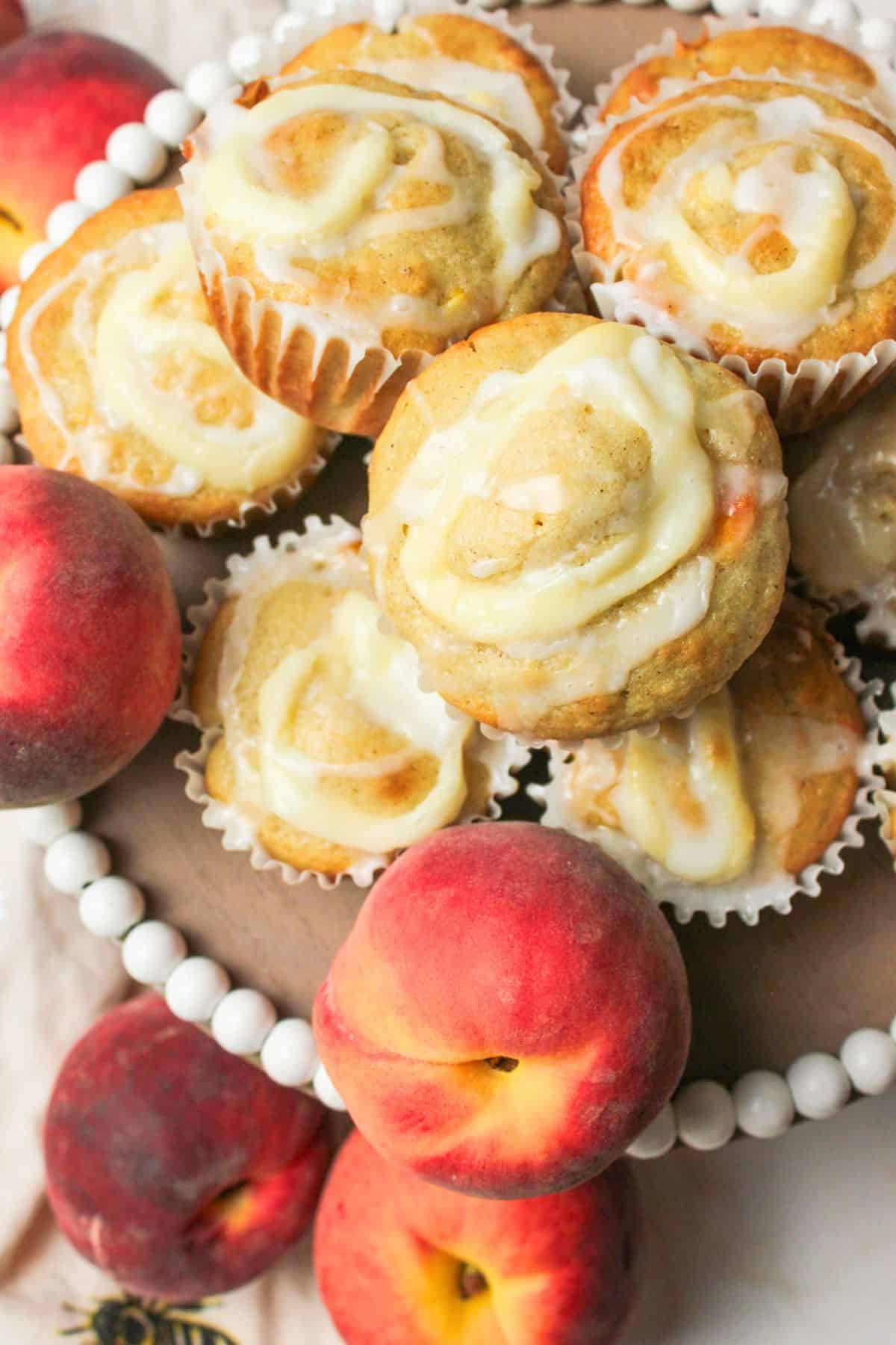 peaches and cream muffins on a plate with fresh peaches.