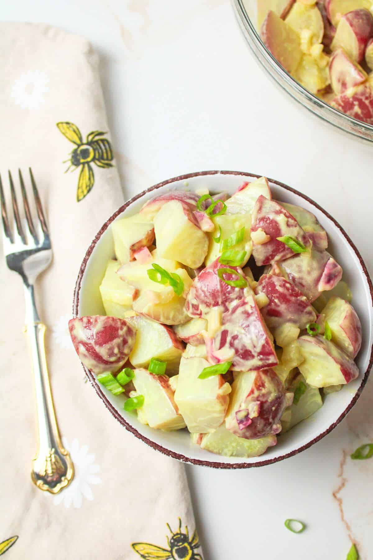 red potato salad in a bowl with green onions.