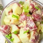 red potato salad in a bowl topped with green onions.