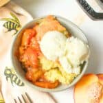 peach cobbler in a bowl with ice cream on top.