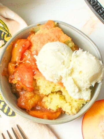 peach cobbler in a bowl with ice cream on top.