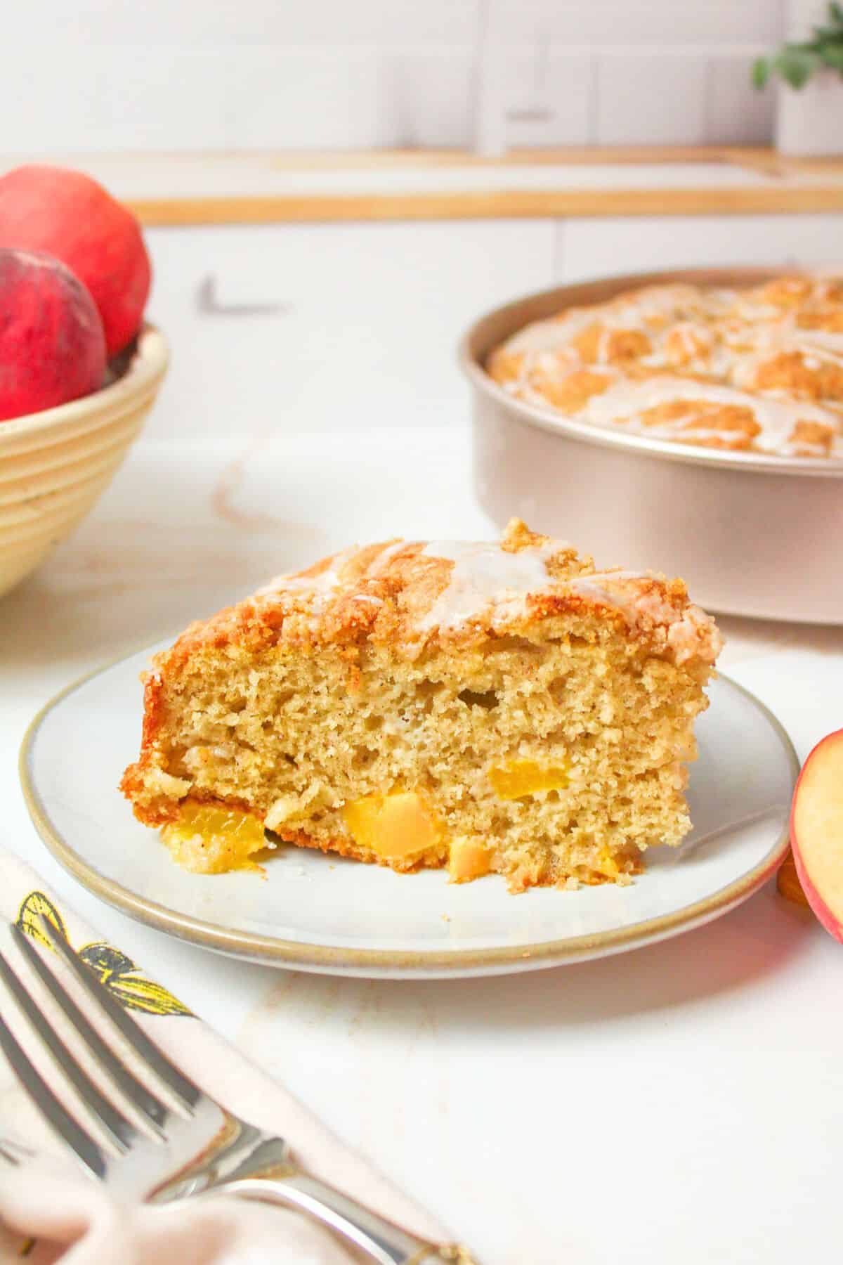 sliced peach coffee cake on a plate with more in background.