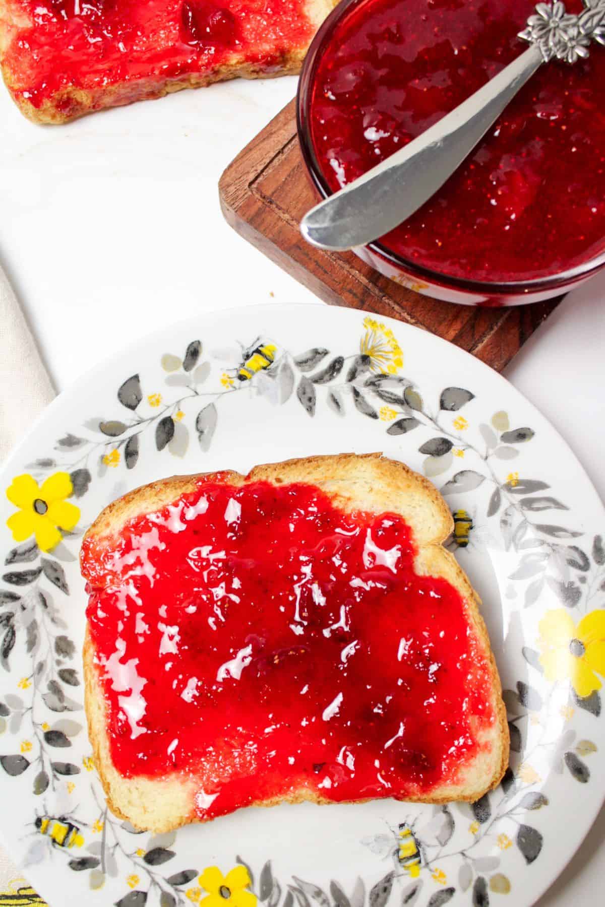 strawberry jam on a piece of toast on a plate.