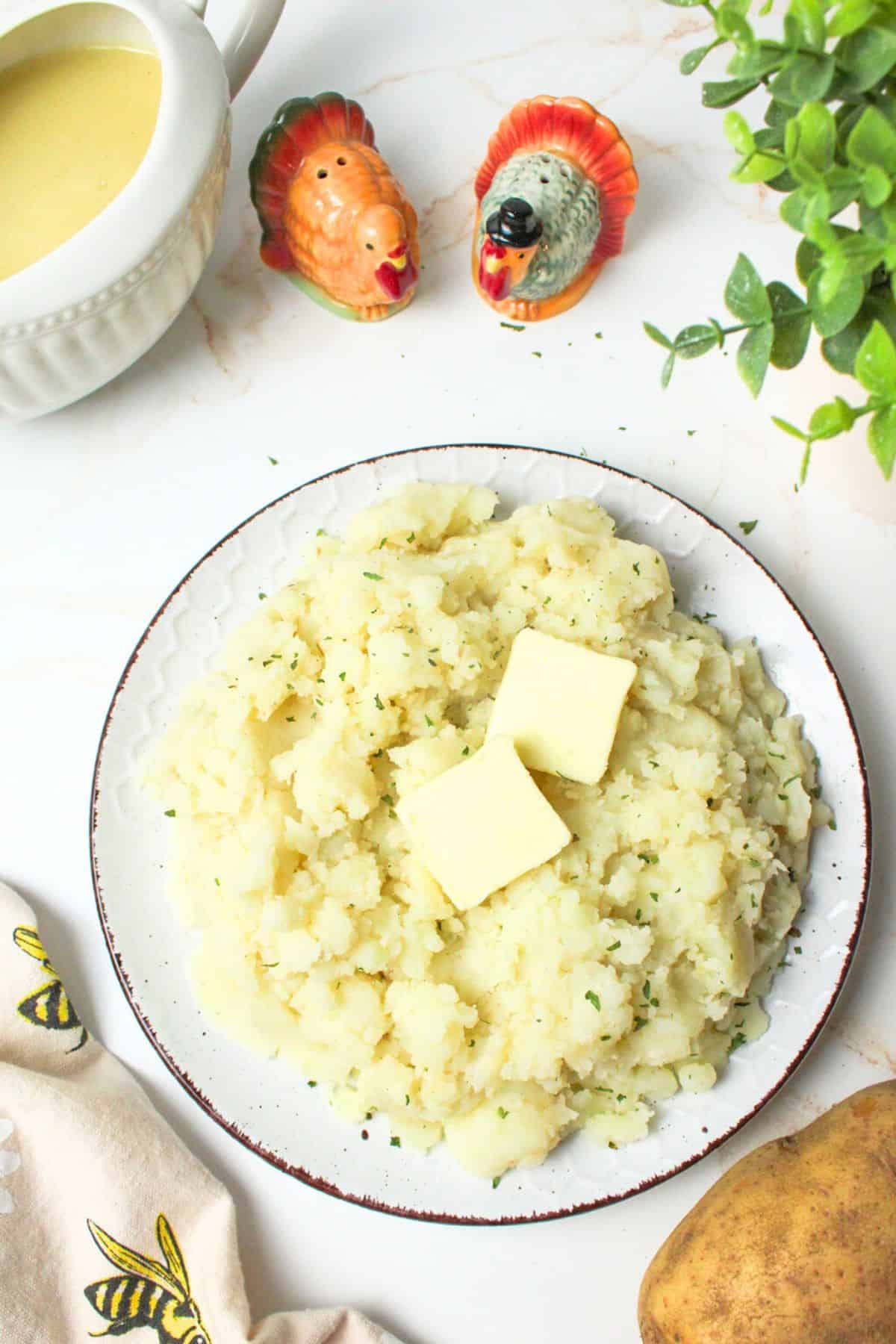 dairy free mashed potatoes on a plate topped with butter and parsley.