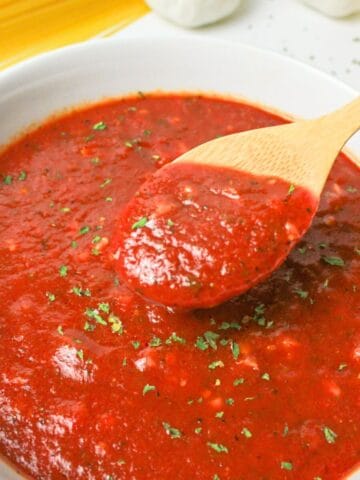 a wooden spoon lifting a bite of spaghetti sauce from the bowl.