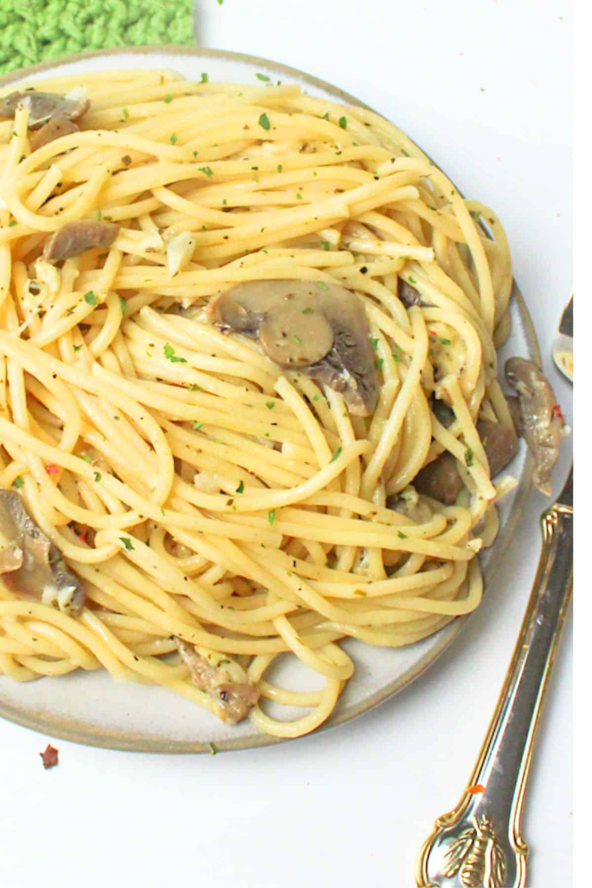 mushroom garlic spaghetti on a plate with a for beside it.