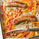 roasted bell pepper and onions on a baking sheet with cooked brats.