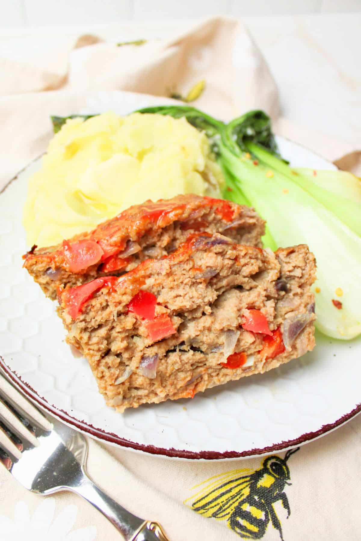 sliced turkey meatloaf on a plate with mashed potatoes and bok choy.