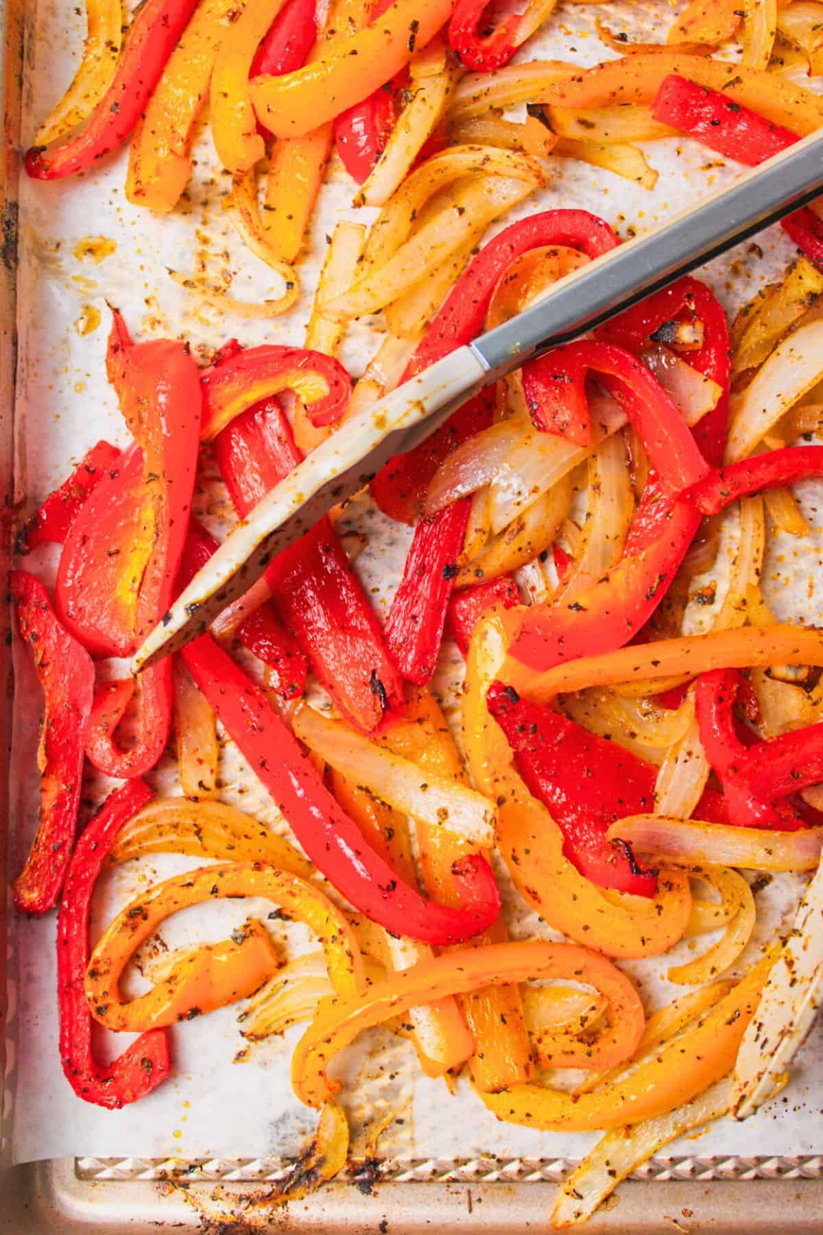roasted bell peppers and onions on a baking heet with tongs.