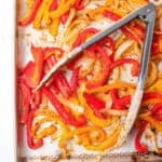 roasted peppers and onion on a baking sheet with tongs.