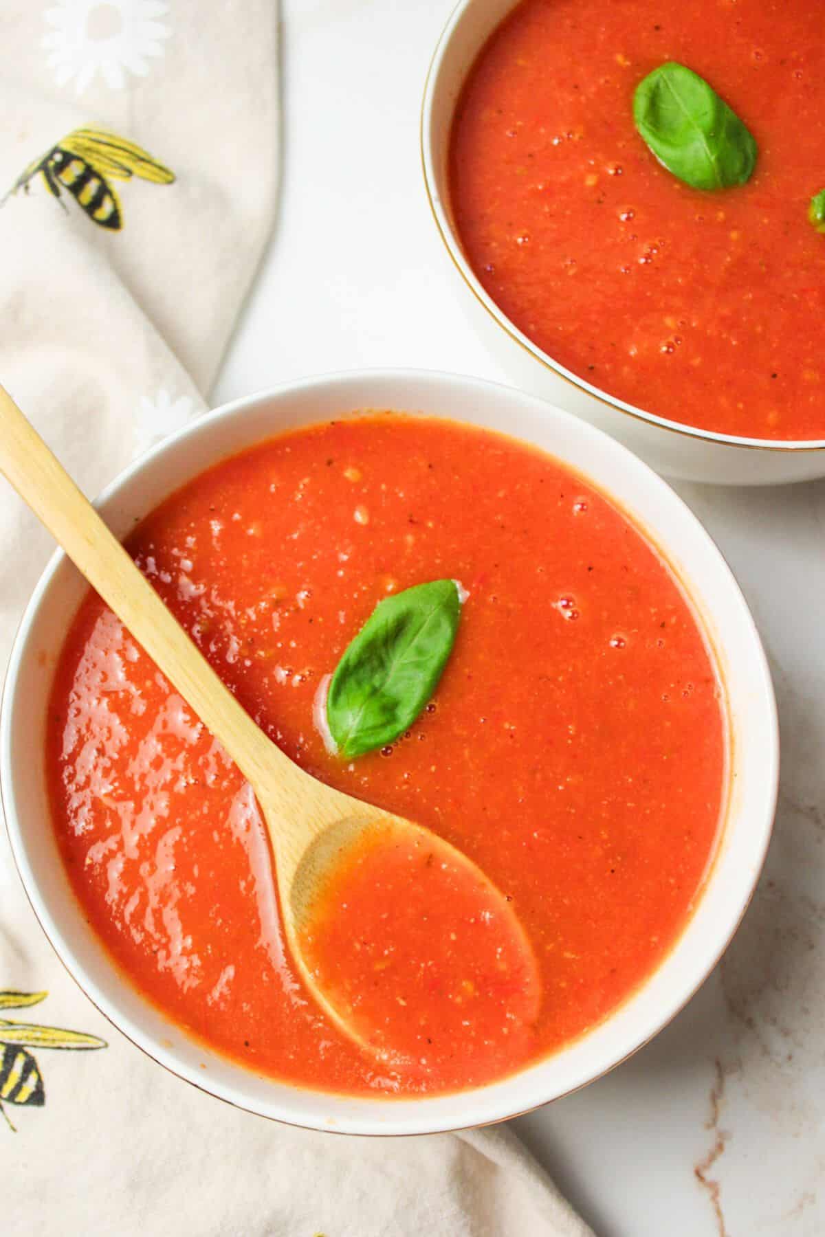 two bowls of tomato soup, one with a wooden spoon inside.