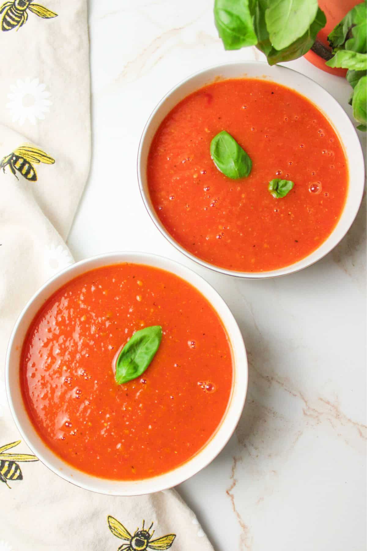 two bowls of tomato soup with basil leaves for garnish.
