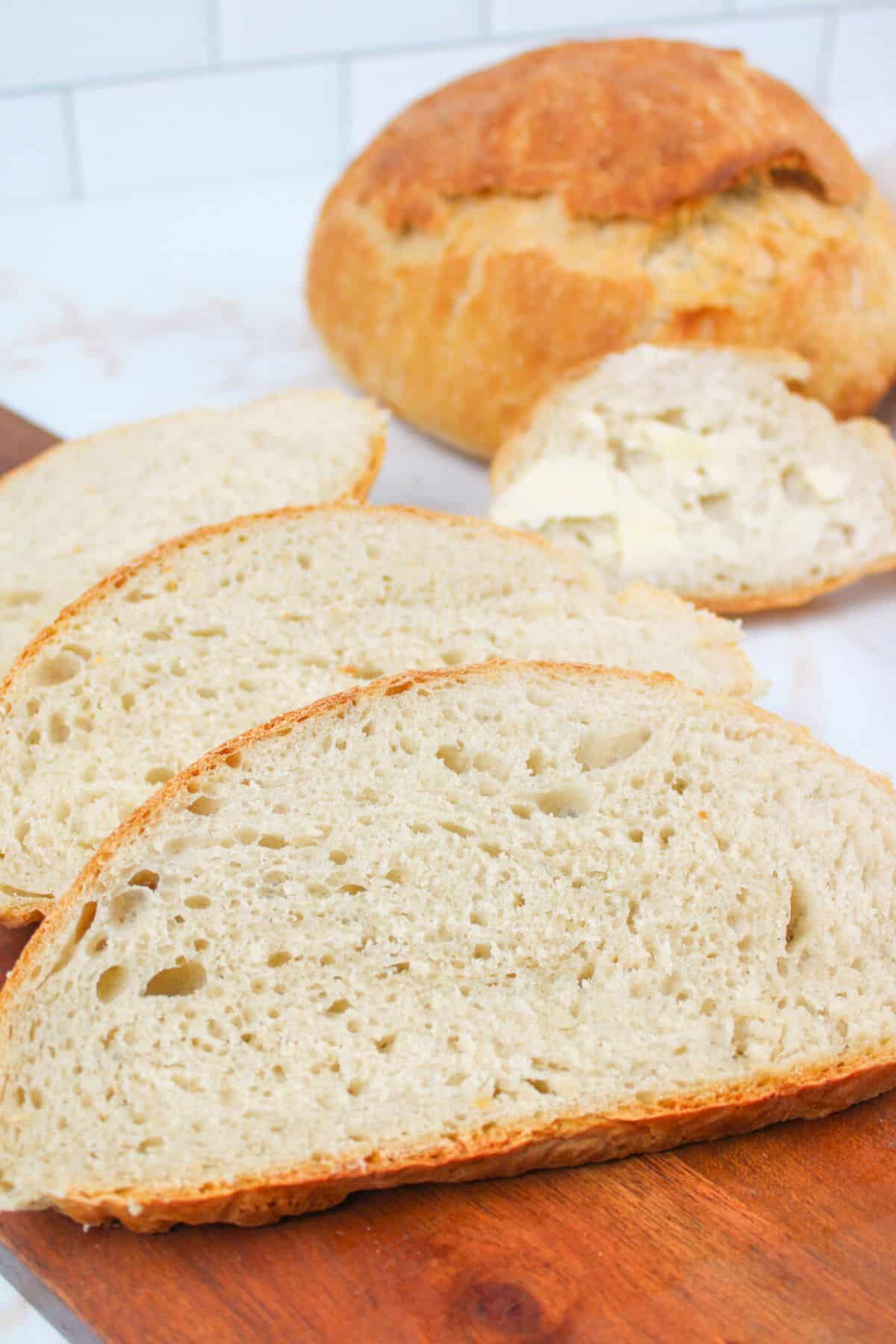 sliced no knead bread on wooden cutting board.
