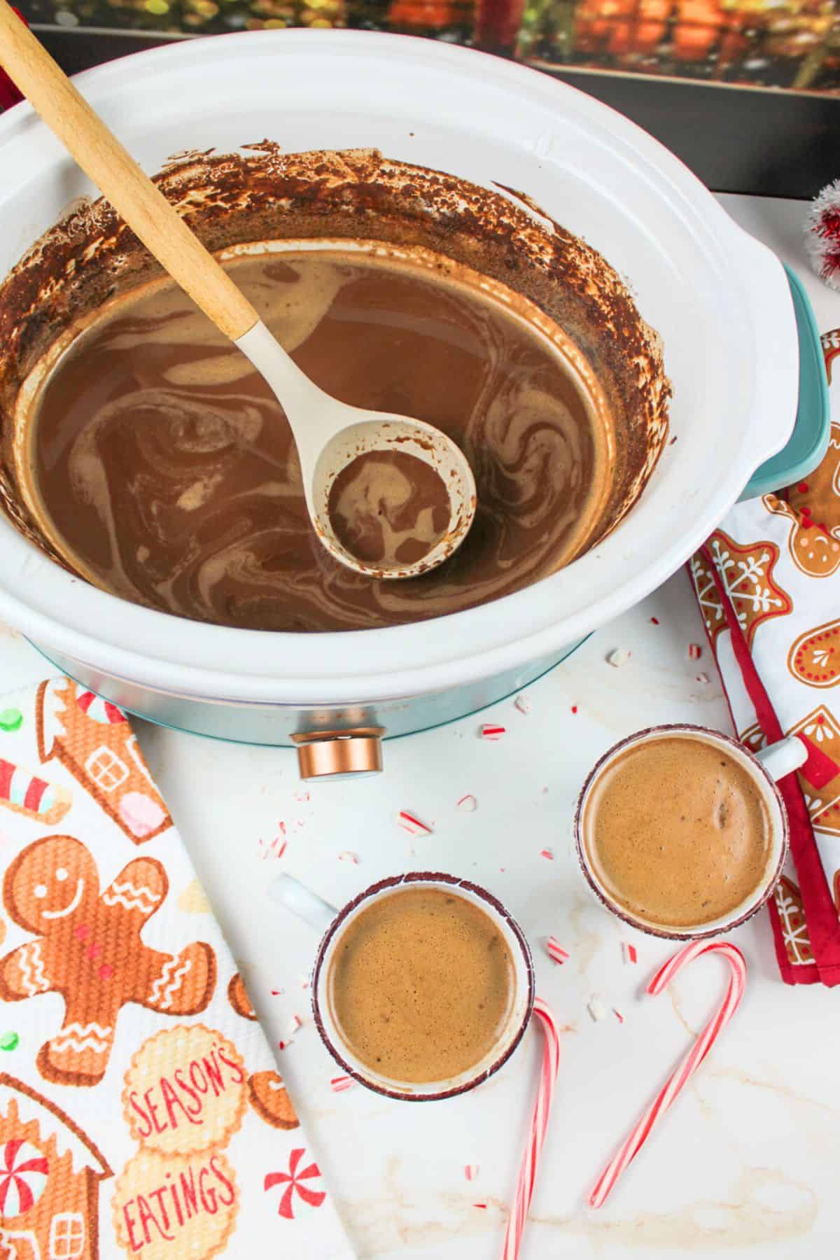 two mugs of cocoa next to a crockpot with more inside.