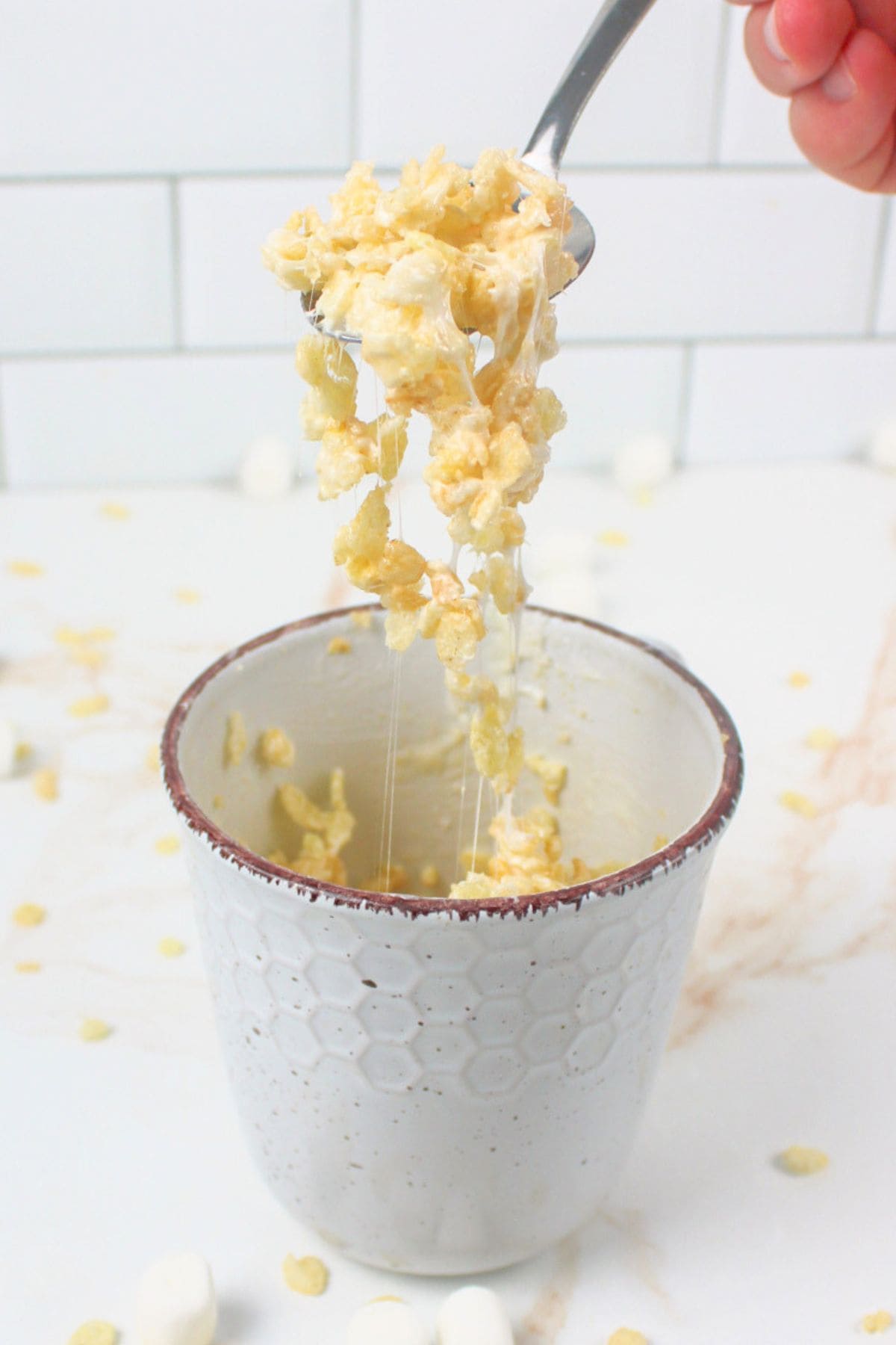 a spoon pulling gooey krispie treat from a mug.