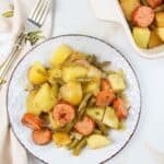 sausage green bean potato casserole on a white plate with a fork to the side.