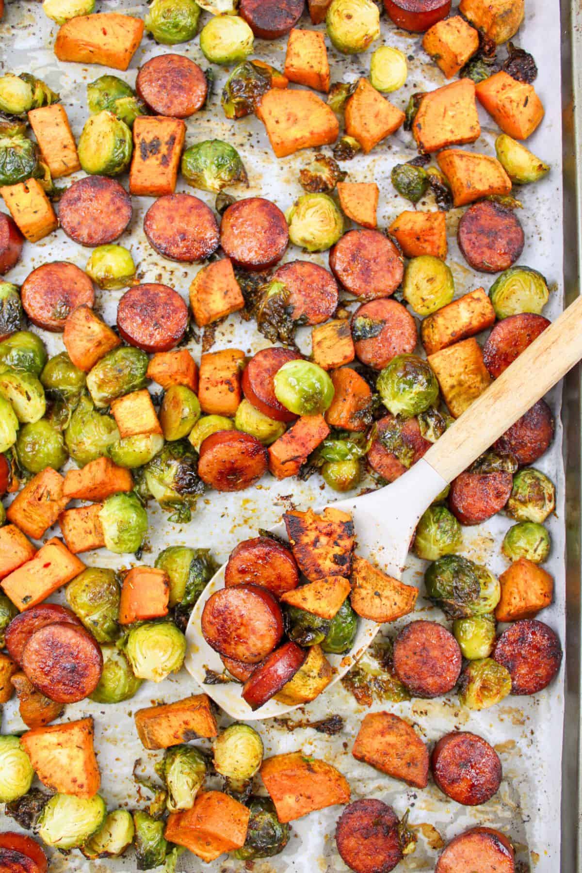 a serving spoon on a sheet pan with sausage and brussels sprouts.
