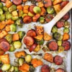 serving spoon on a sheet pan with sausages and brussels sprouts.