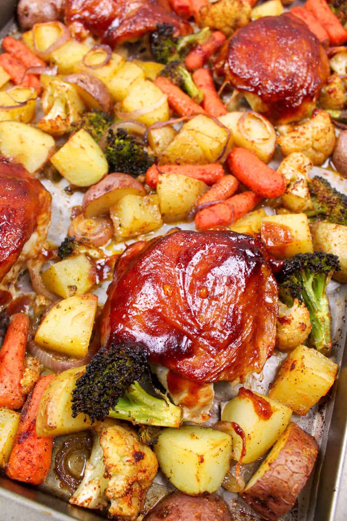 bbq chicken thigh with potatoes and veggies on a baking sheet.