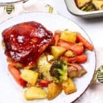 bbq chicken thigh on a plate with potatoes and veggies.