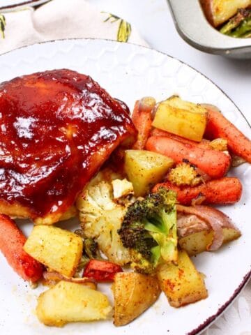 bbq chicken thigh on a plate with potatoes and veggies.