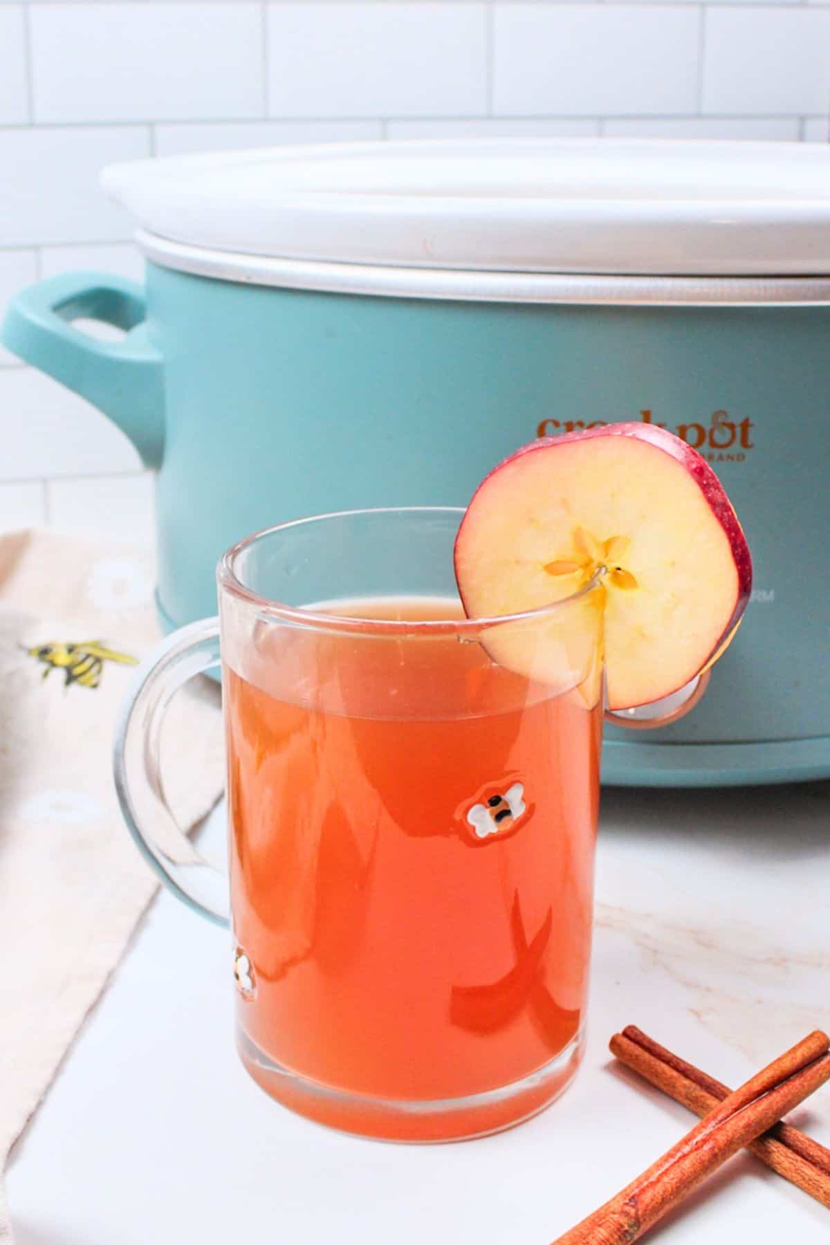 apple cider ina glass mug in front of crockpot.