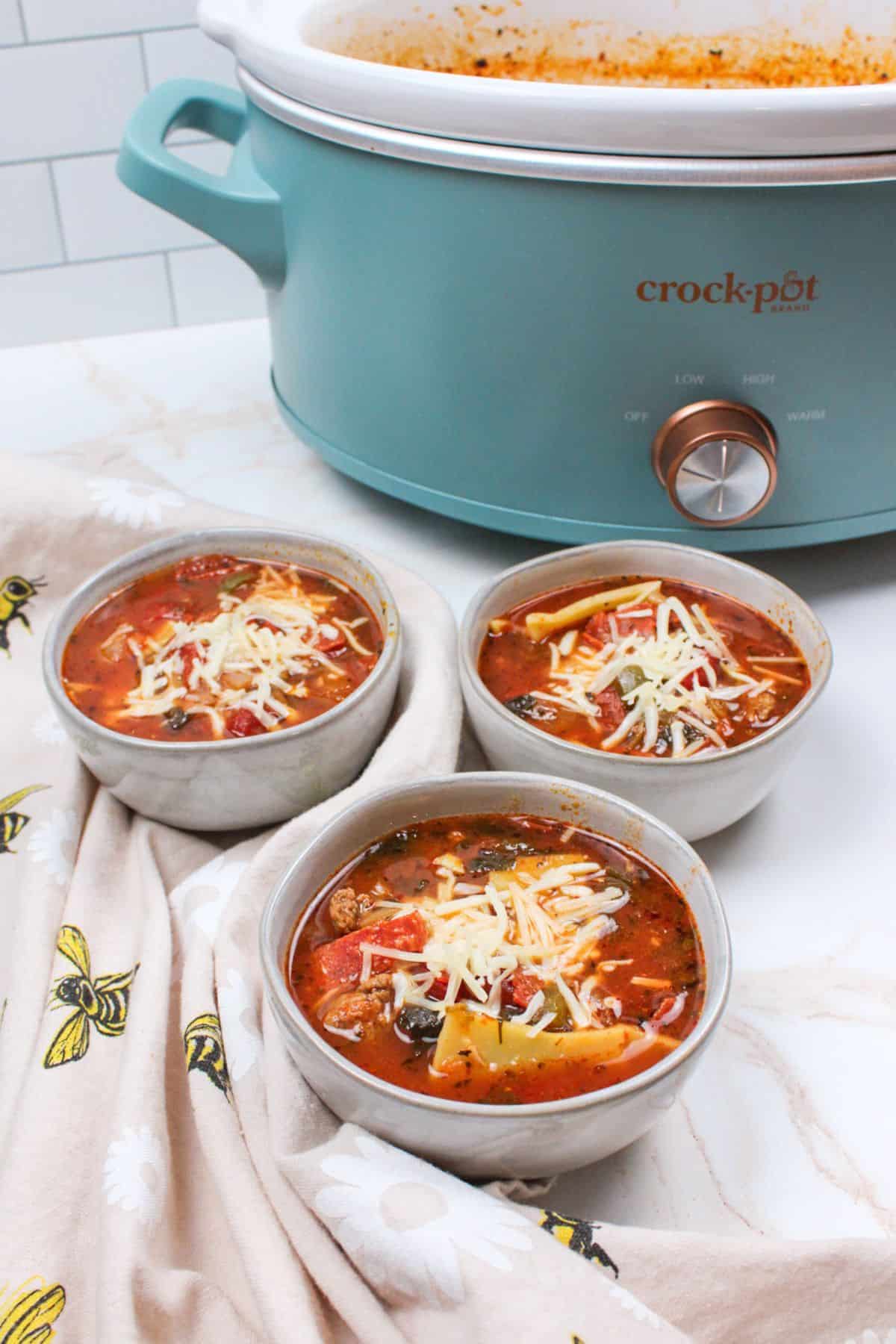 pizza soup in bowls with cheese on top and crockpot in background.