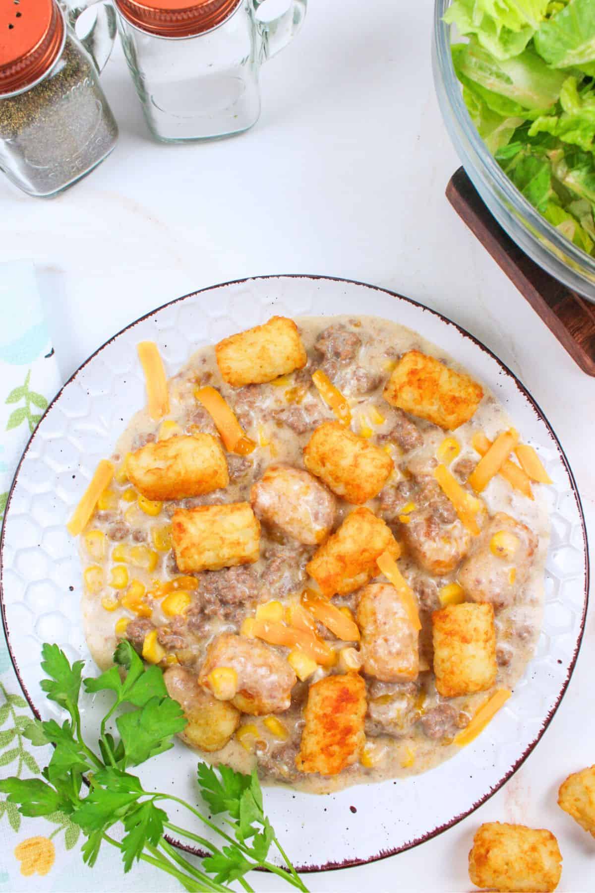 tater tot casserole served on plate next to salad and salt and pepper shakers.