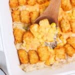 a wooden spoon digging into tater tot corn casserole in baking dish.