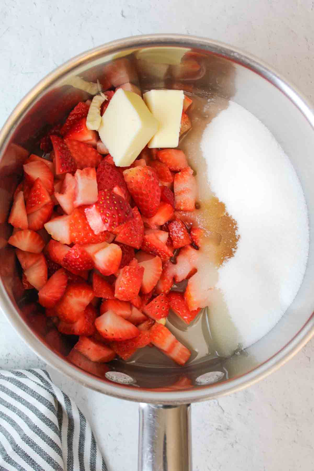 a bowl filled with sugar, vanilla, sliced strawberries, and butter.
